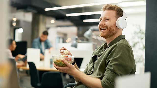 Male employee smiling and eating a health lunch at his desk.