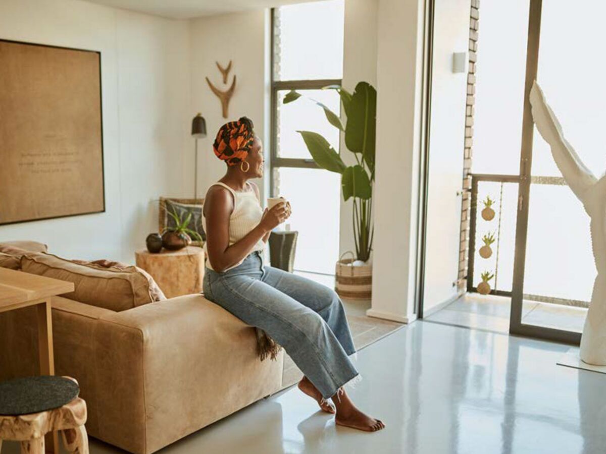 woman sitting on the edge of the couch drinking coffee while looking out the window
