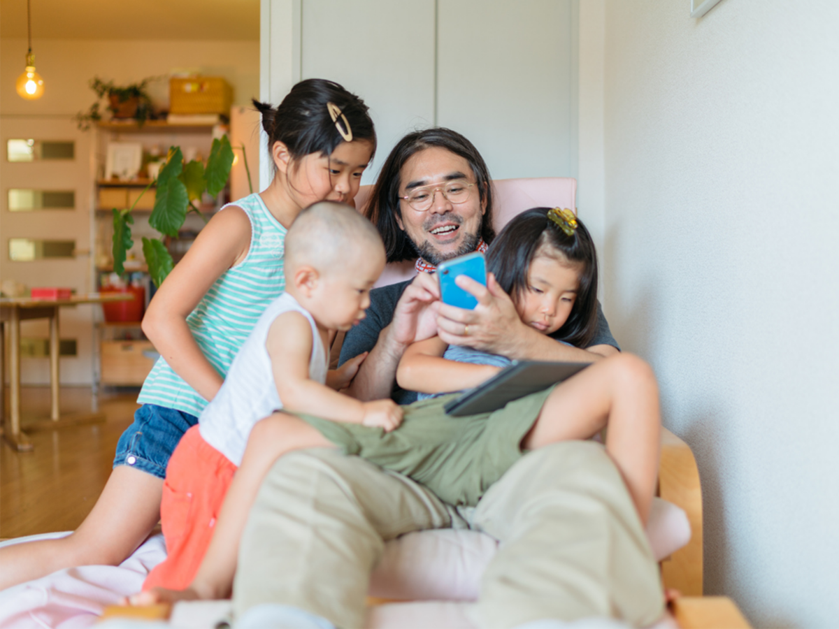 Father on his phone while his kids climb on him
