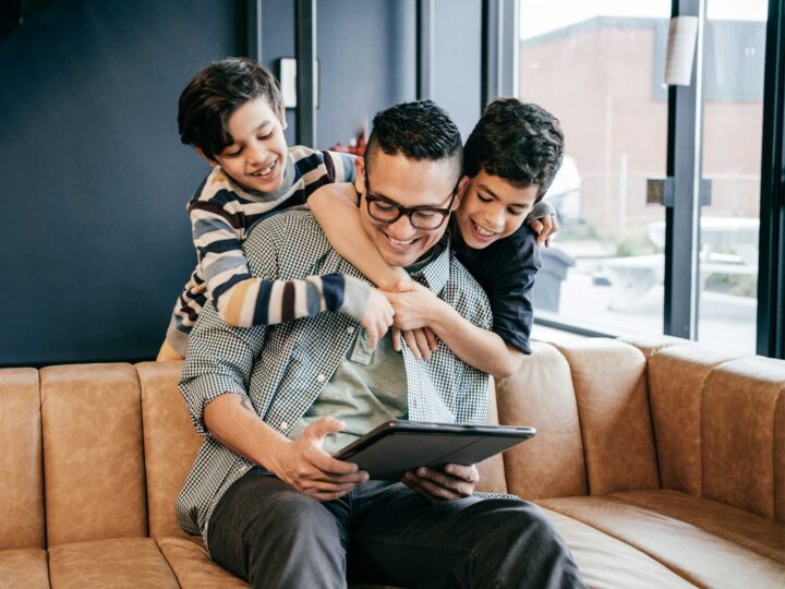 Father and two sons smiling on the couch while looking at a tablet