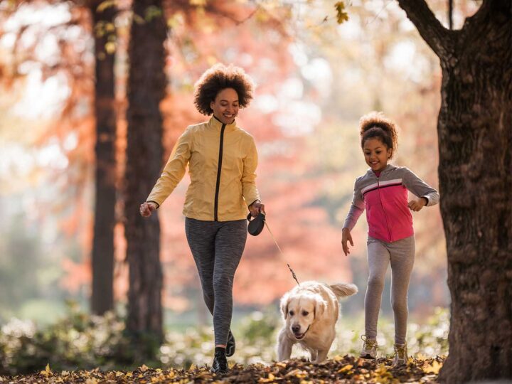 woman and daughter walking their dog in the trees during fall