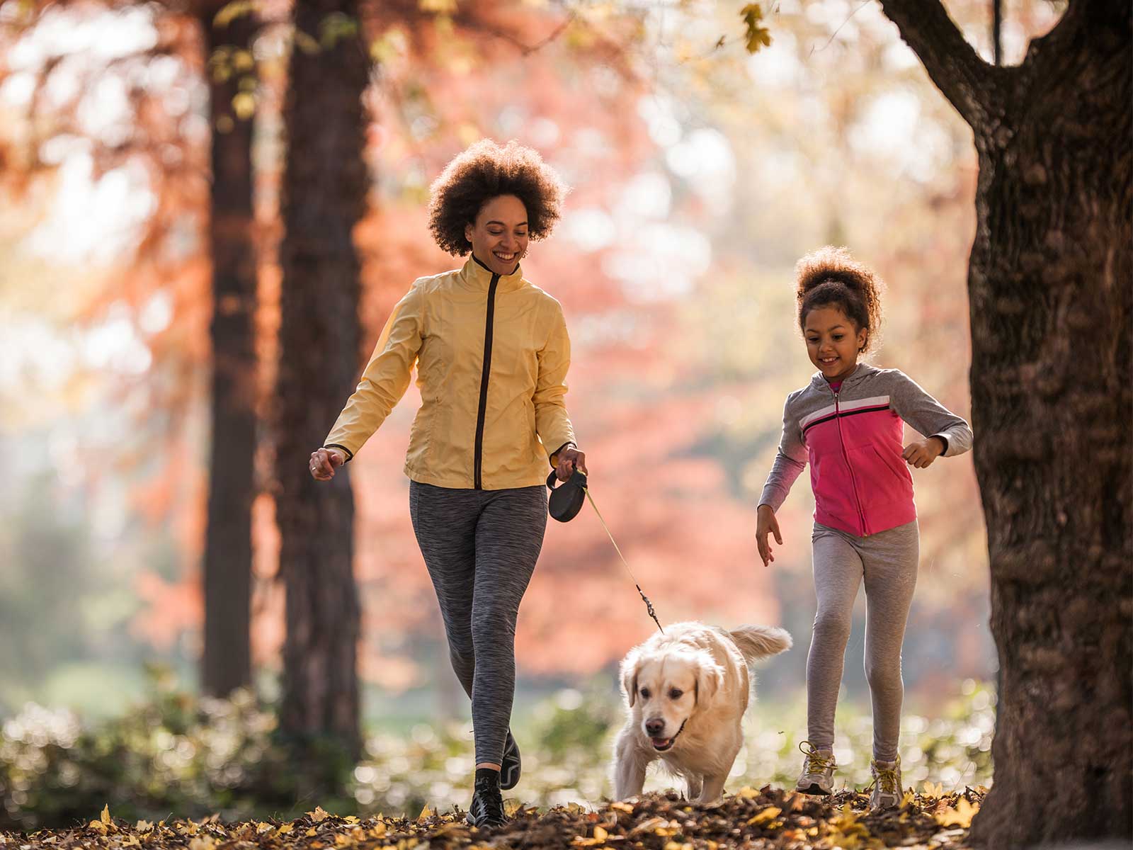 woman and daughter walking their dog in the trees during fall