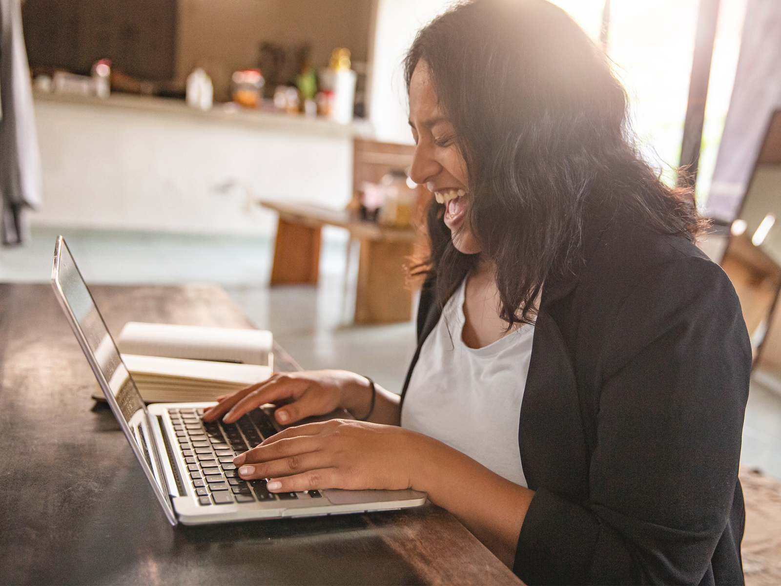 Female laughing while typing on her laptop in her house