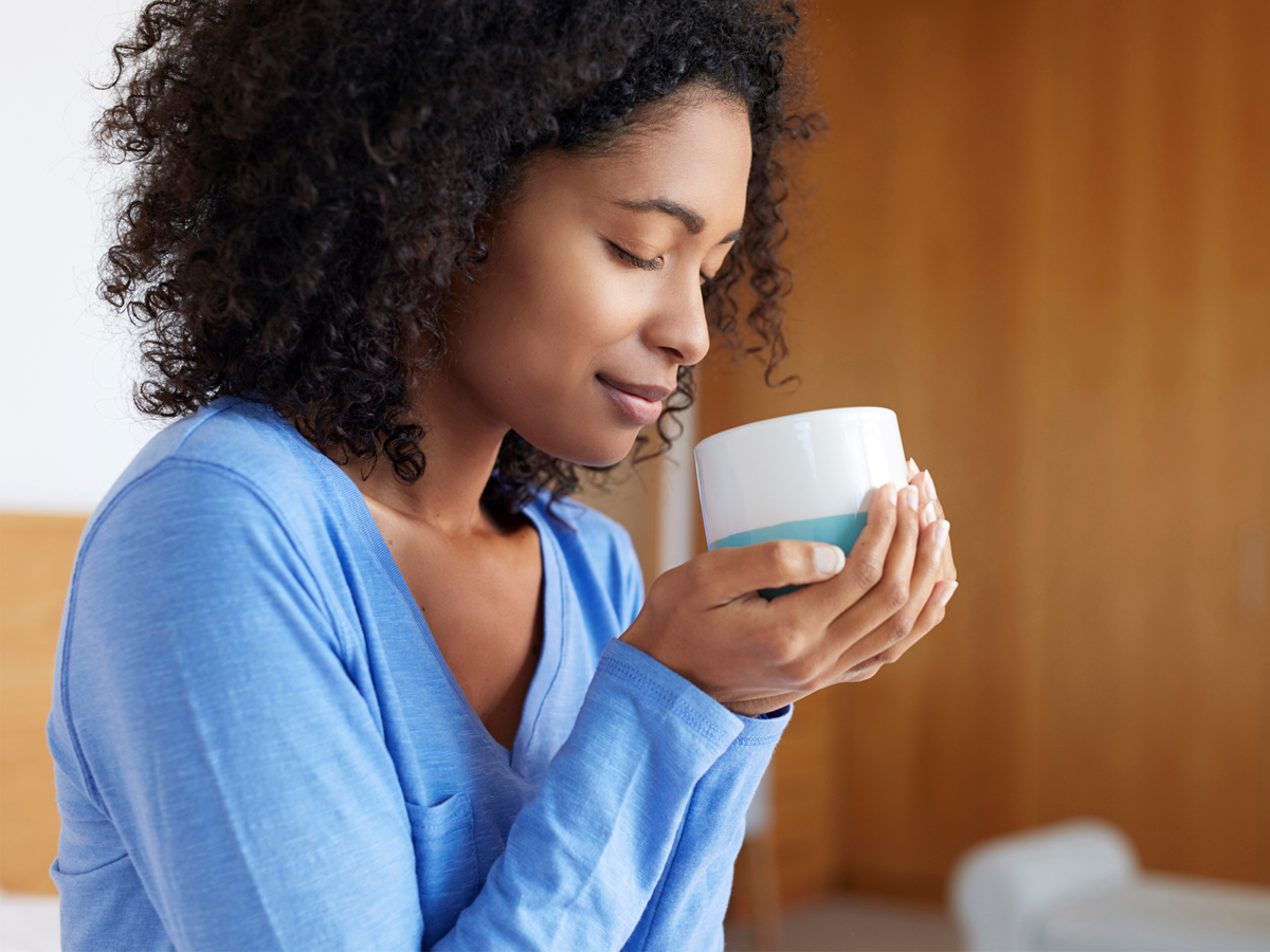 woman with closed eyes smelling her cup of coffee