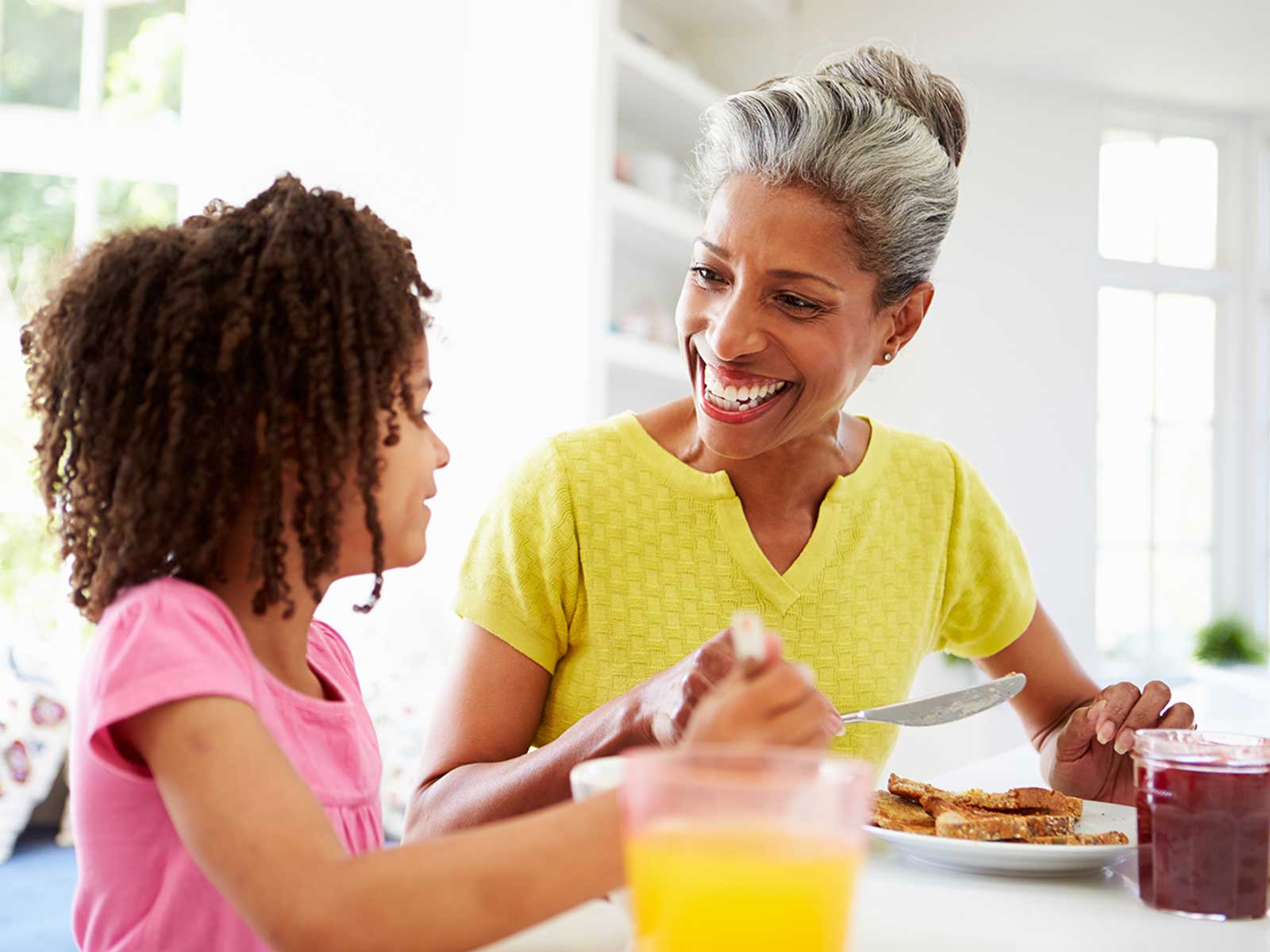 Grandma smiling and eating breakfast with her granddaughter