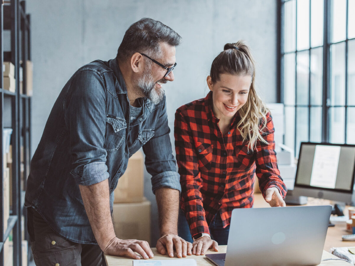 two employees smiling while looking at a laptop