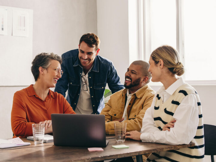 group of employees sitting around a laptop smiling
