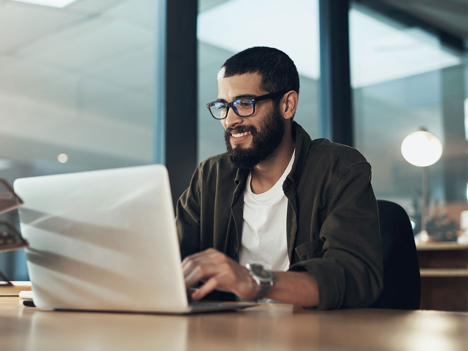 man smiling while sitting at his desk looking at his laptop