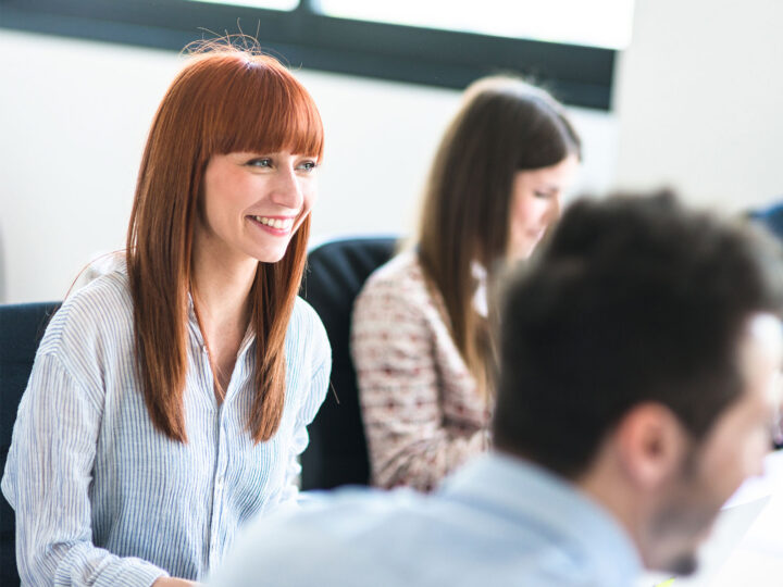 engaged female employee smiling while sitting with colleagues
