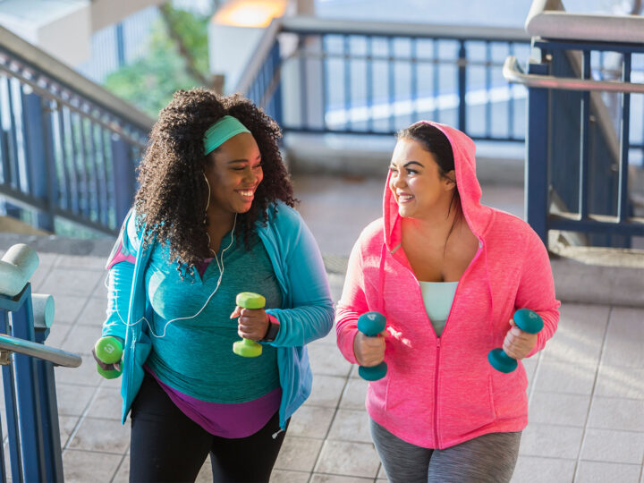 two women holding dumbbells and walking up steps