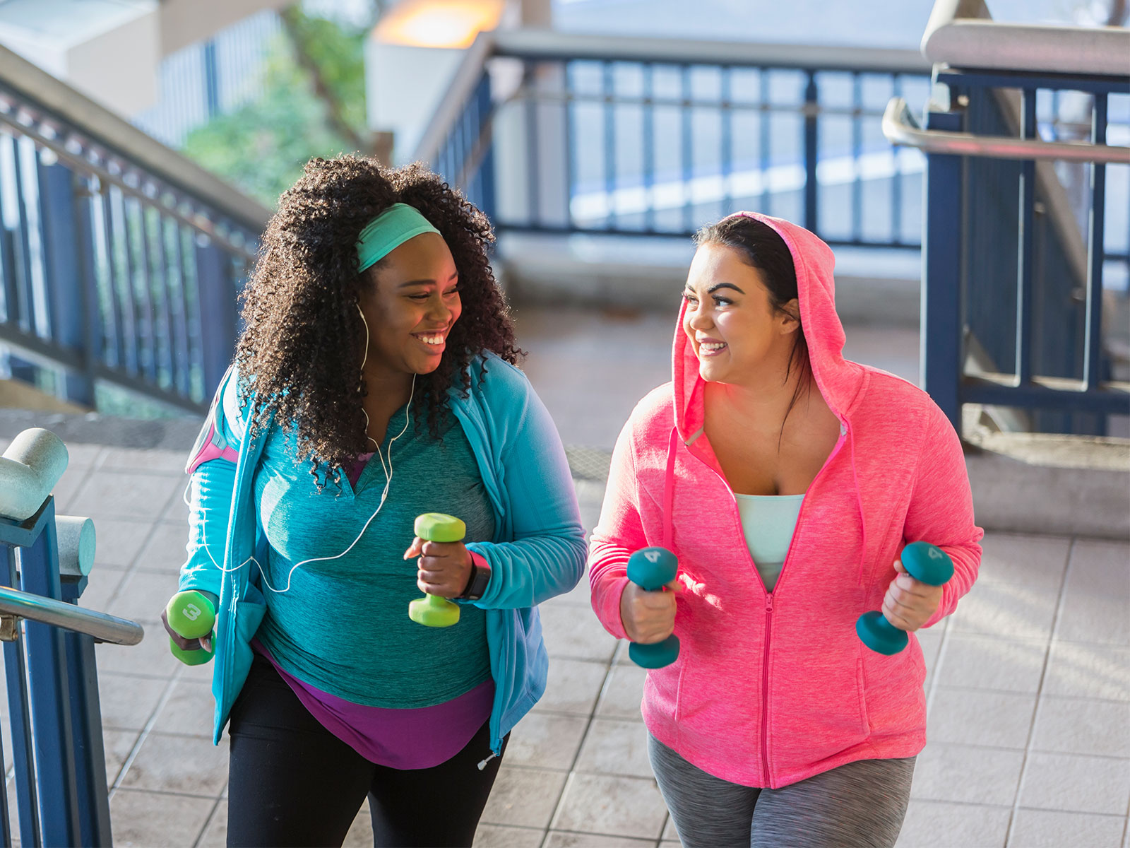 two women holding dumbbells and walking up steps