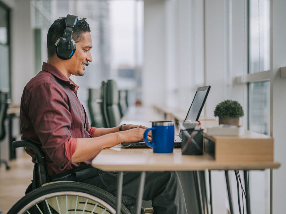 male employee in a wheel chair with headphones on looking at his laptop