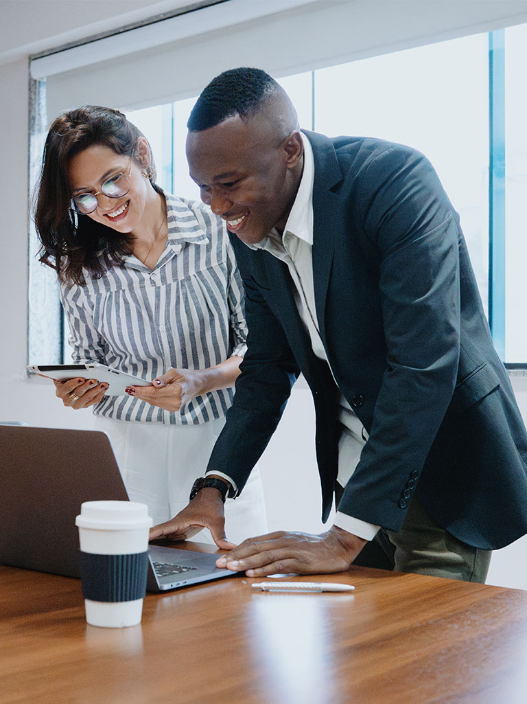 male and female employee smiling while looking at a laptop