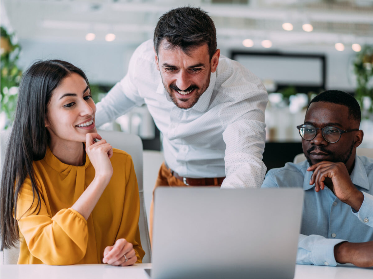 Three employees smiling while looking at a laptop