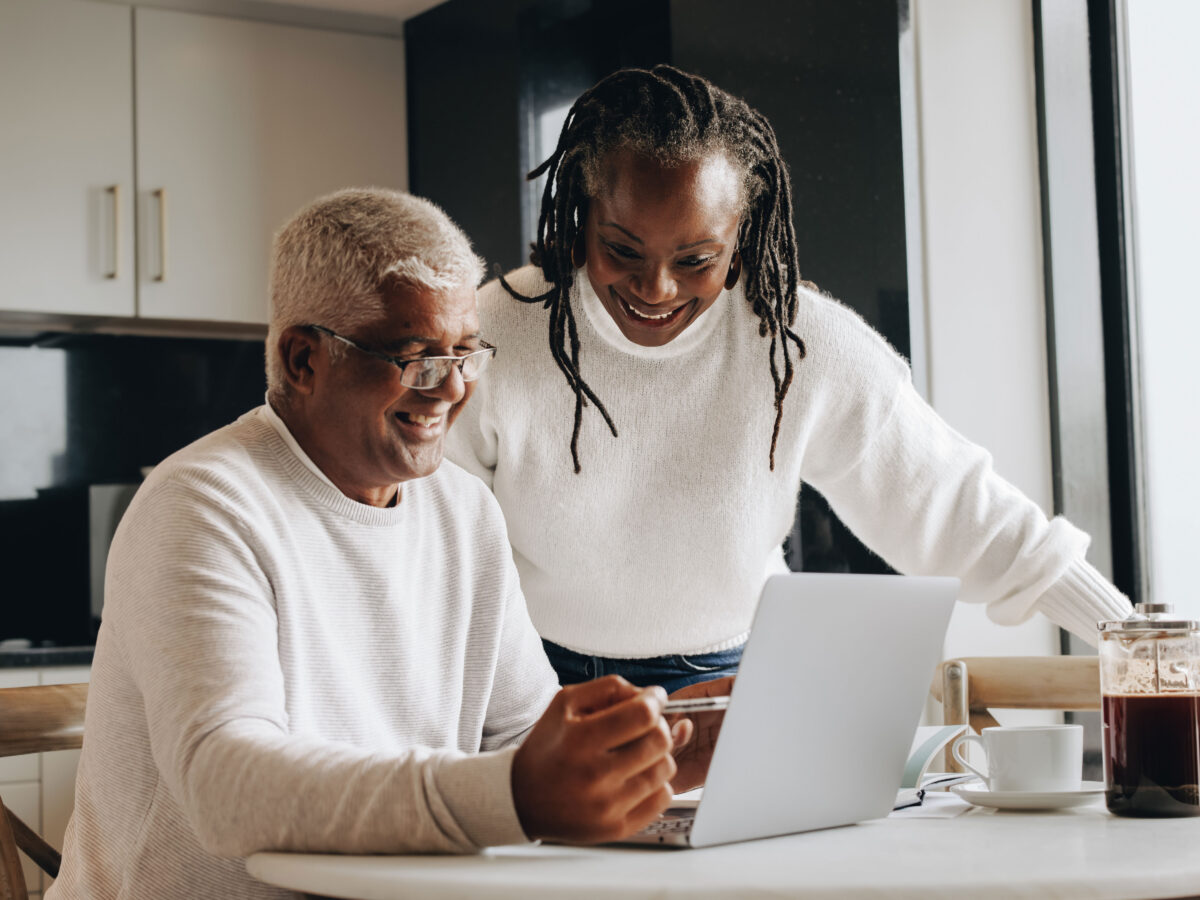 husband and wife smiling while looking at their finances on their laptop